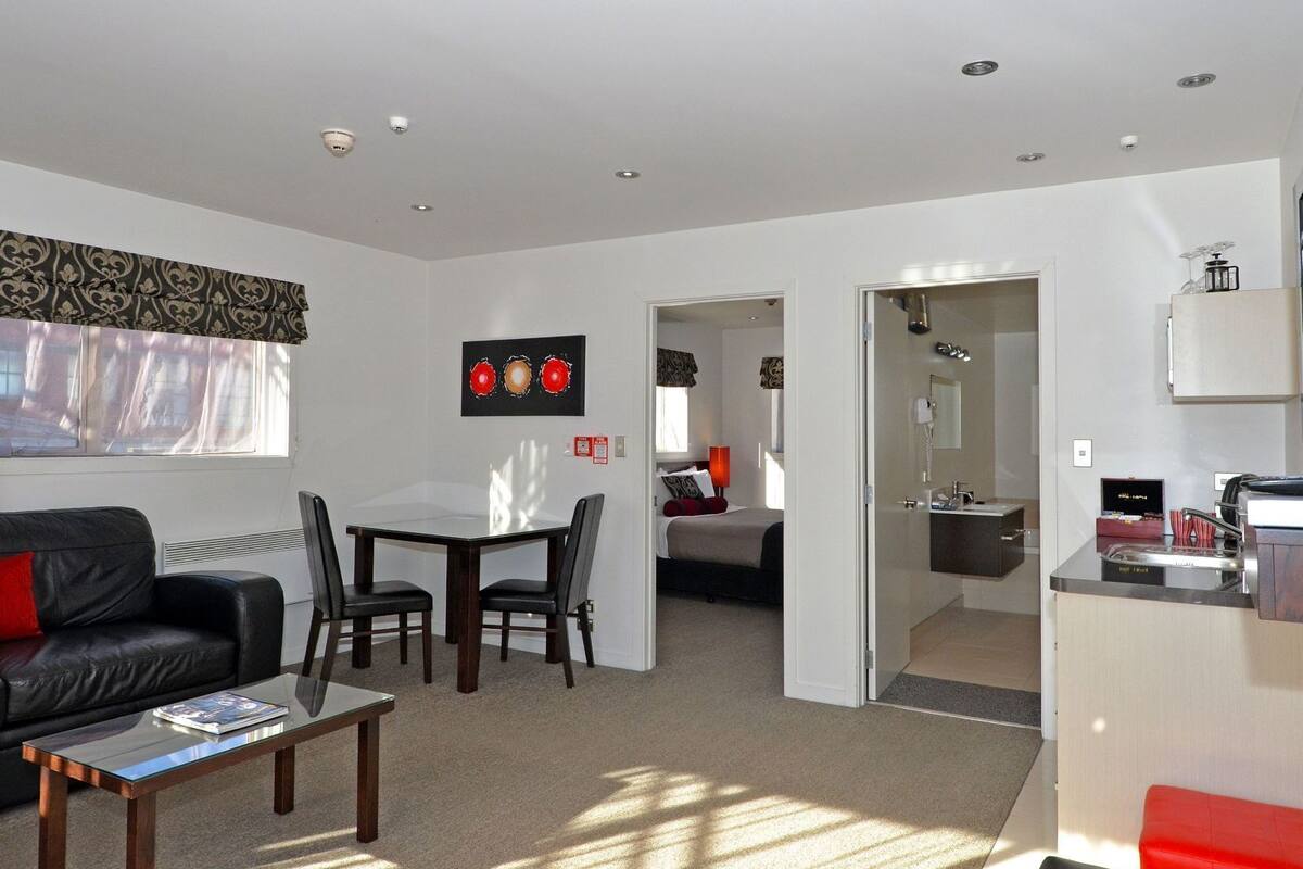 A hotel room with a dining area, a separate bedroom, a bathroom, and a kitchenette.