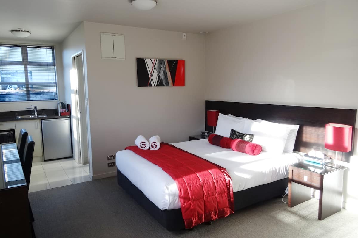 A modern hotel room with a bed, a desk, and a kitchenette.