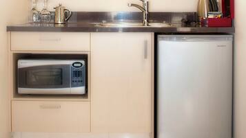 Una cucina compatta con forno a microonde integrato, lavello in acciaio inossidabile e frigorifero compatto.
