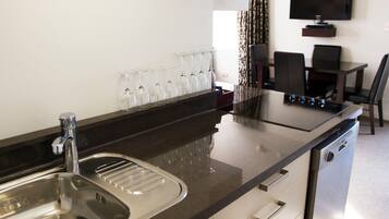 A modern kitchen with a stainless steel sink, a built-in stove, and a flat-screen TV mounted on the wall.