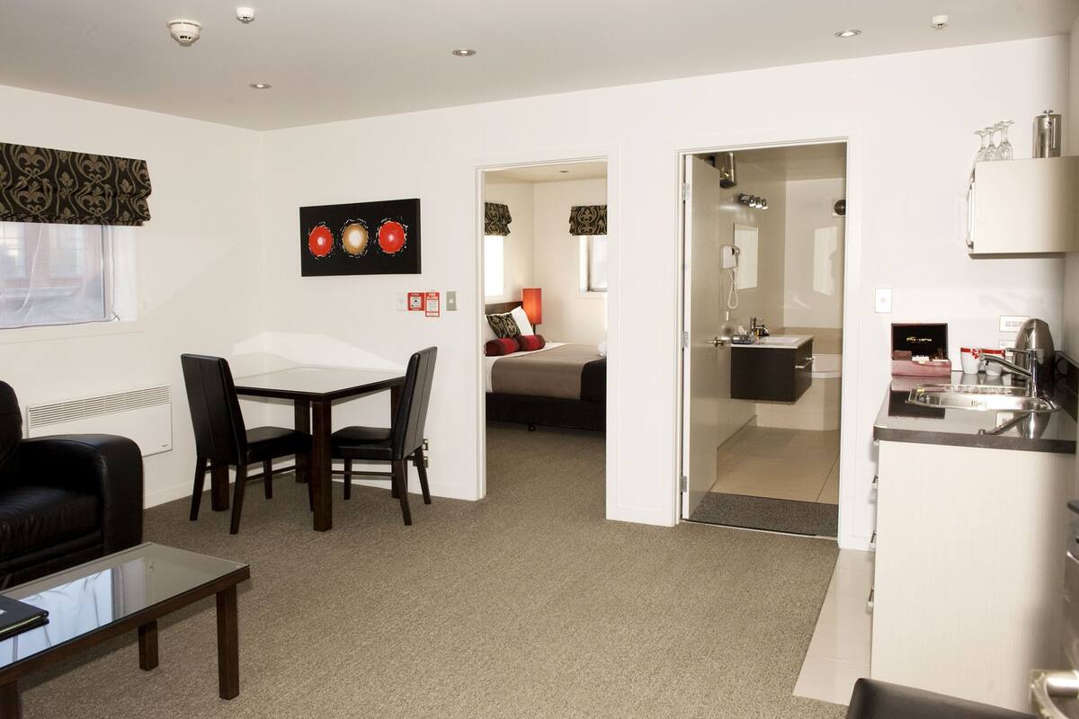 A modern hotel room with a dining area, a bed, a bathroom, and a kitchenette.