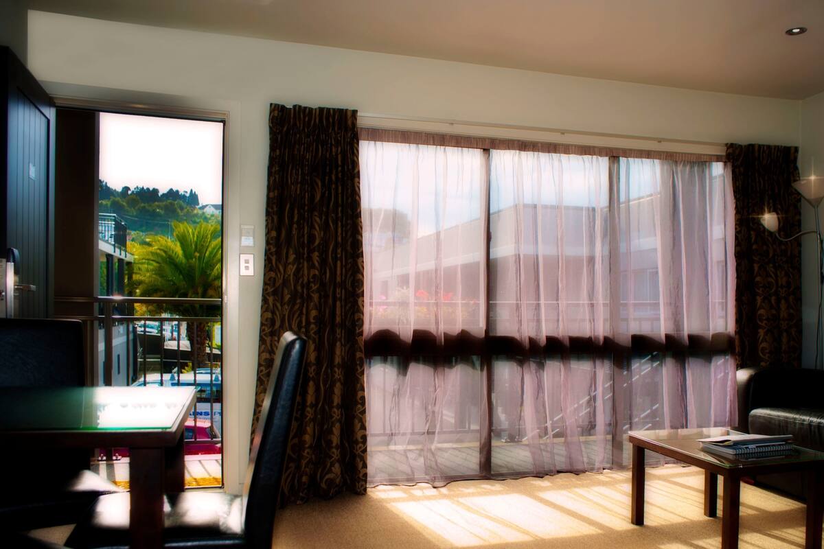 A room with a dining table, chairs, a sofa, and a window with curtains.