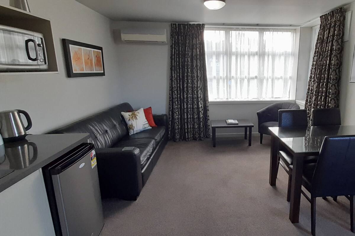 A compact living space with a sofa, dining table, chairs, a TV, and a small kitchenette.