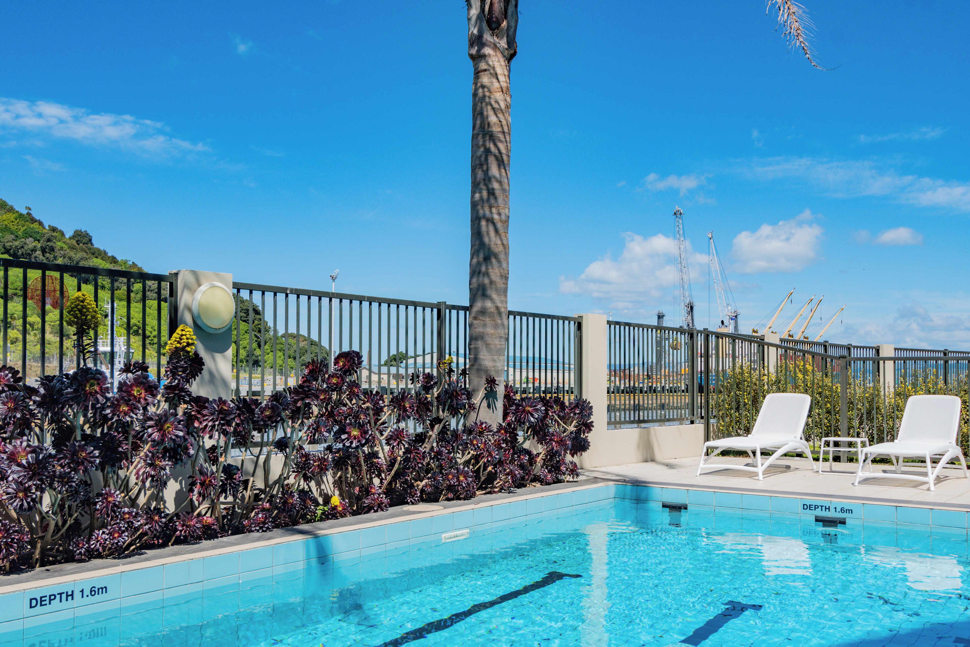A swimming pool with a depth of 1.6 meters, surrounded by a fence, and two white lounge chairs.