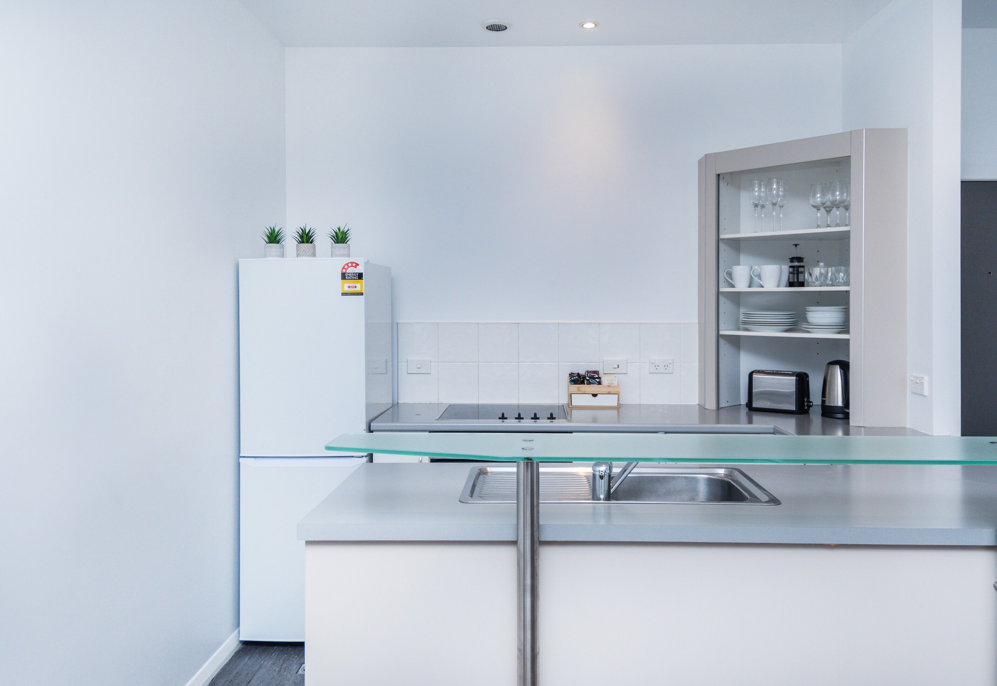 Een moderne keuken met een eiland met glazen blad, roestvrijstalen apparatuur en een inbouw wijnrek.