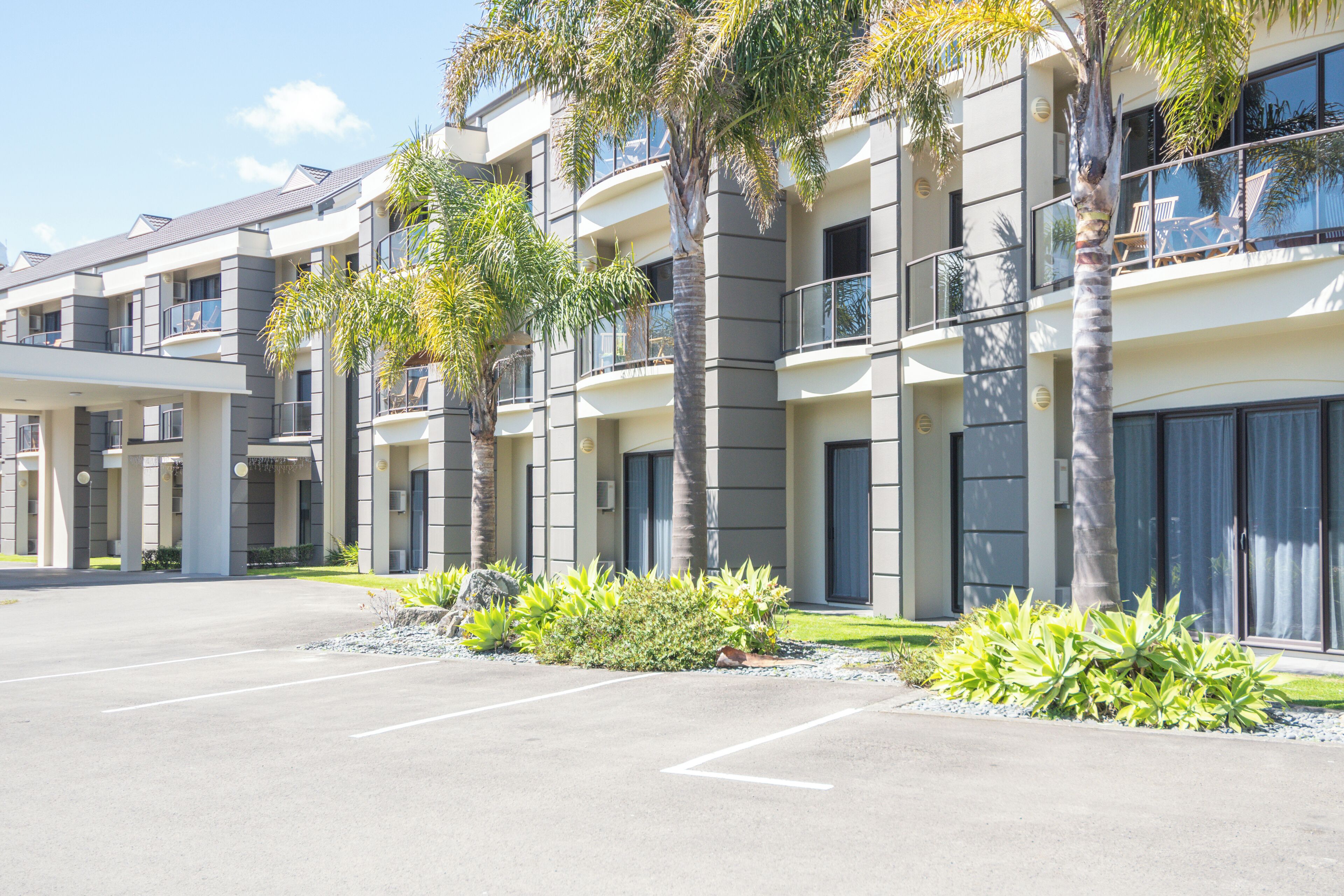 A multi-story hotel with balconies, palm trees, and a parking lot.