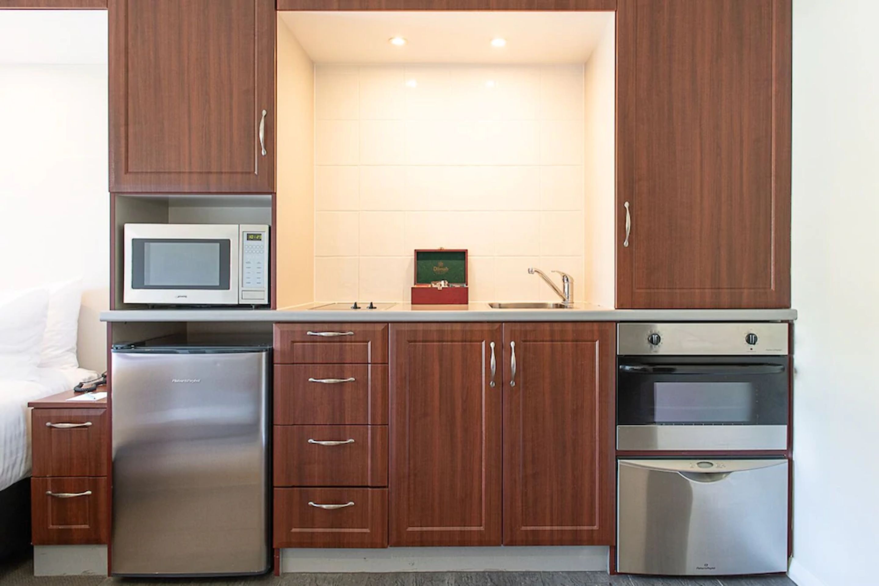 A compact kitchen with a microwave, refrigerator, oven, and wooden cabinets.