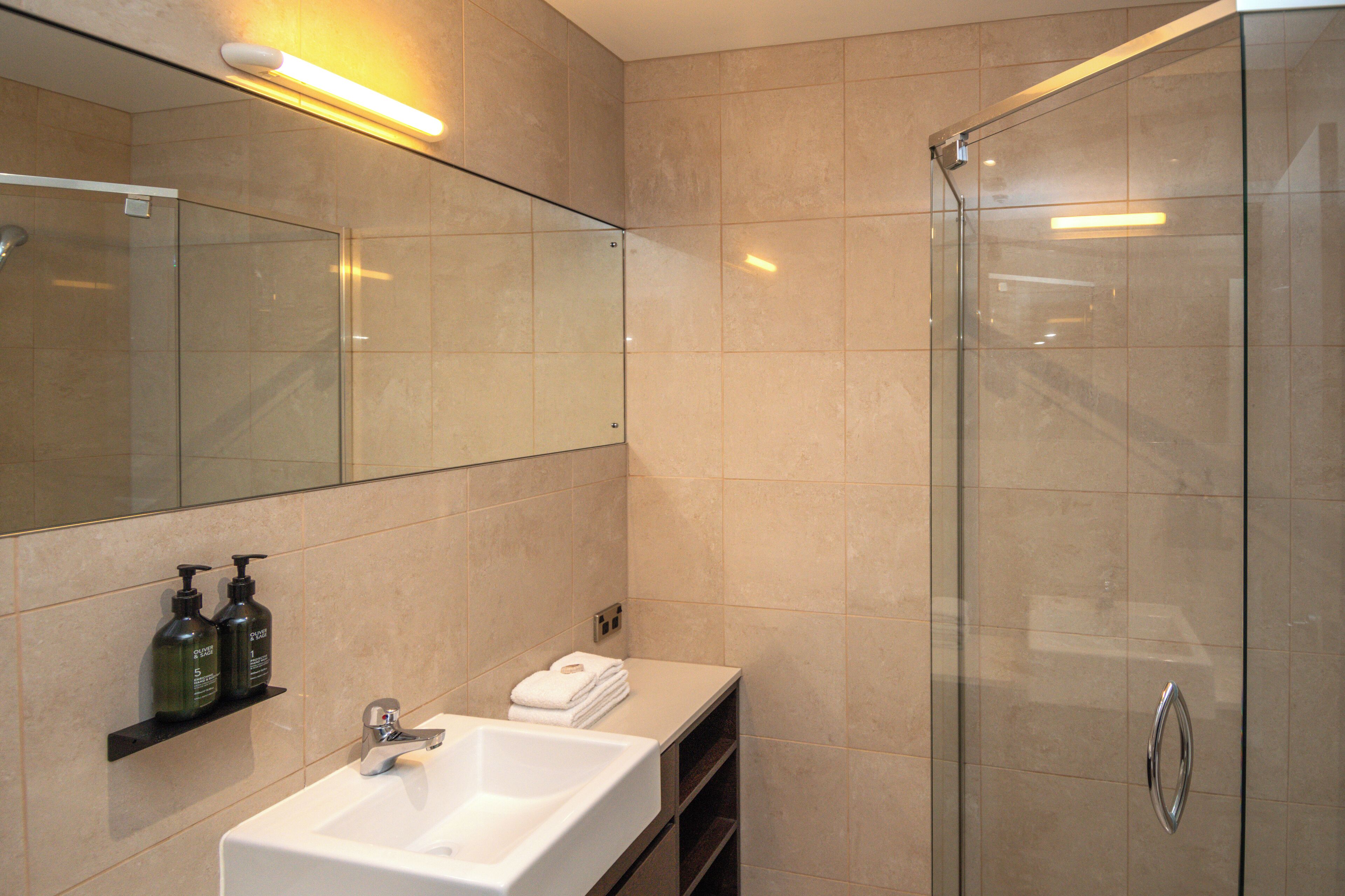 A modern bathroom with a glass shower enclosure, a white sink, and a mirror above it.
