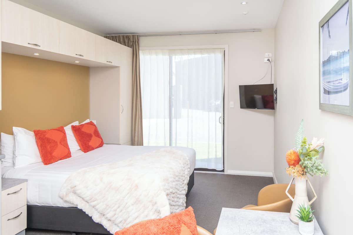 A hotel room with a bed, a desk, a chair, a TV, and a window.