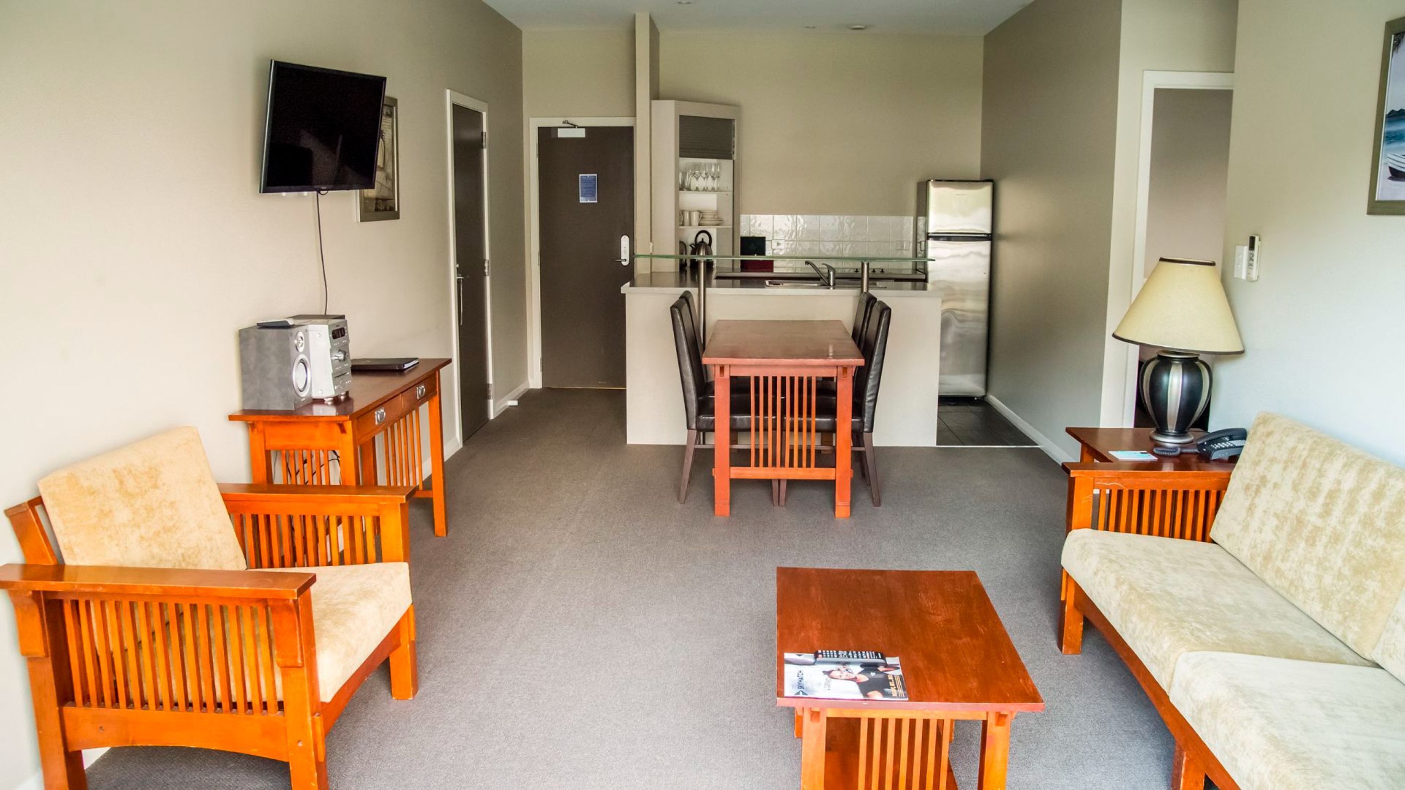Un espacio habitable compacto con un sofá, dos sillones, una mesa de centro, televisor y kitchenette.