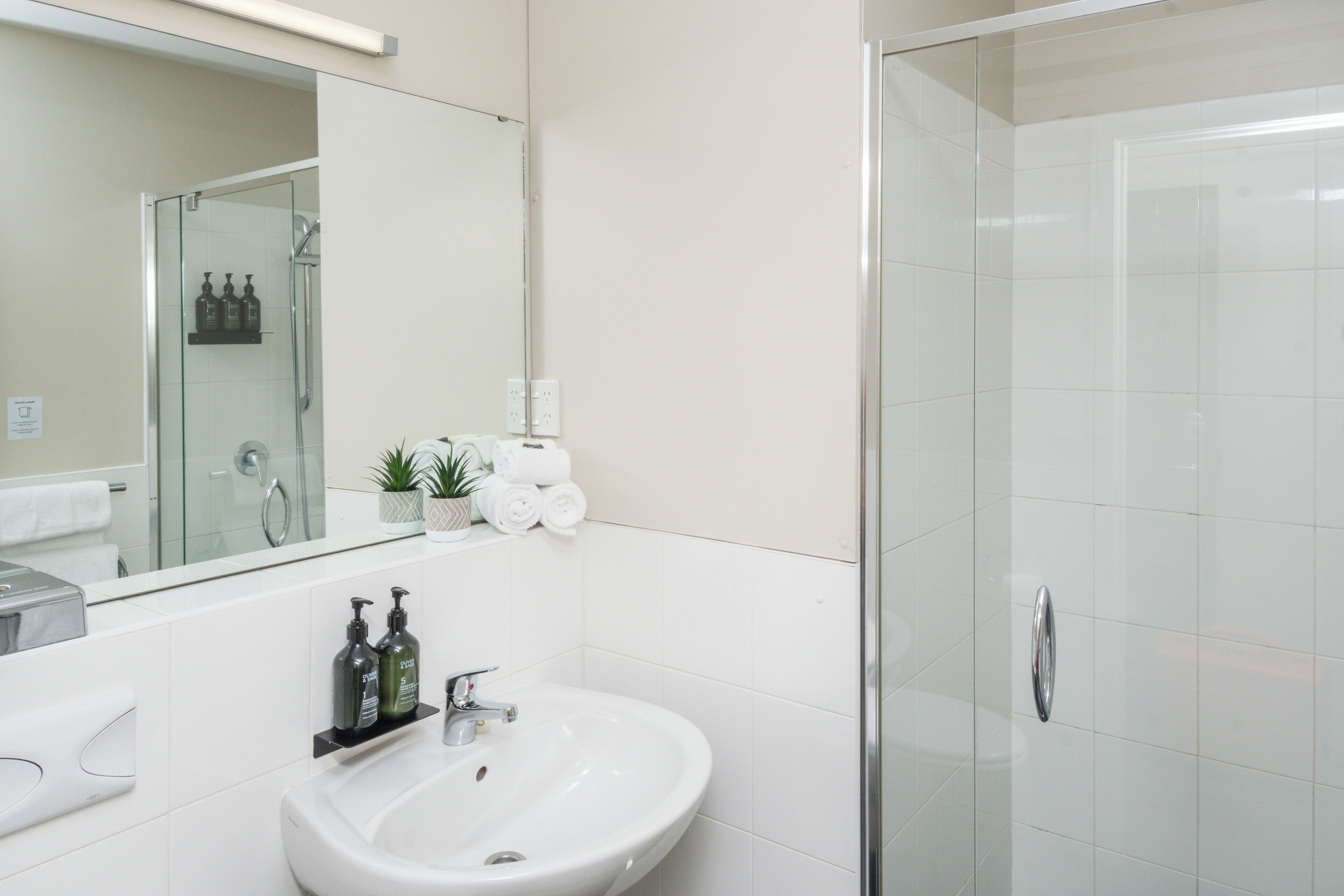 Un bagno moderno con lavandino bianco, specchio e cabina doccia in vetro.