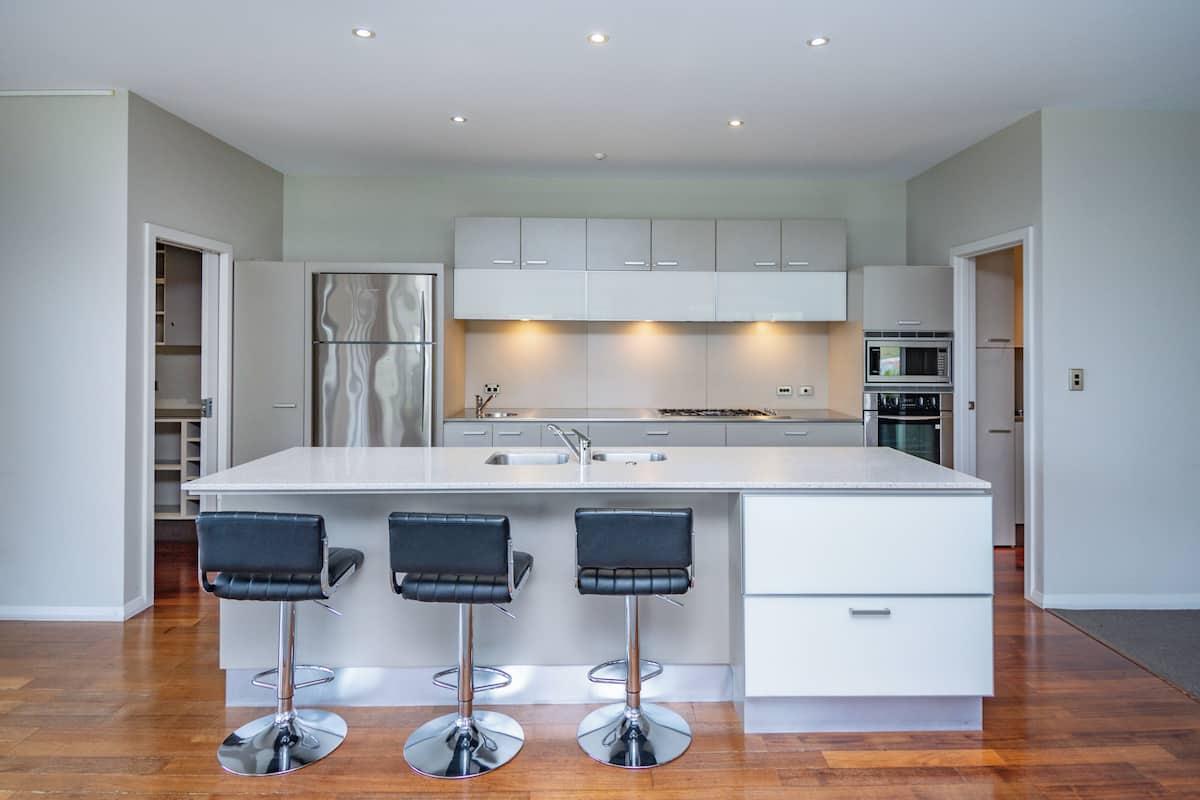 A modern kitchen with a large island, stainless steel appliances, and three bar stools.