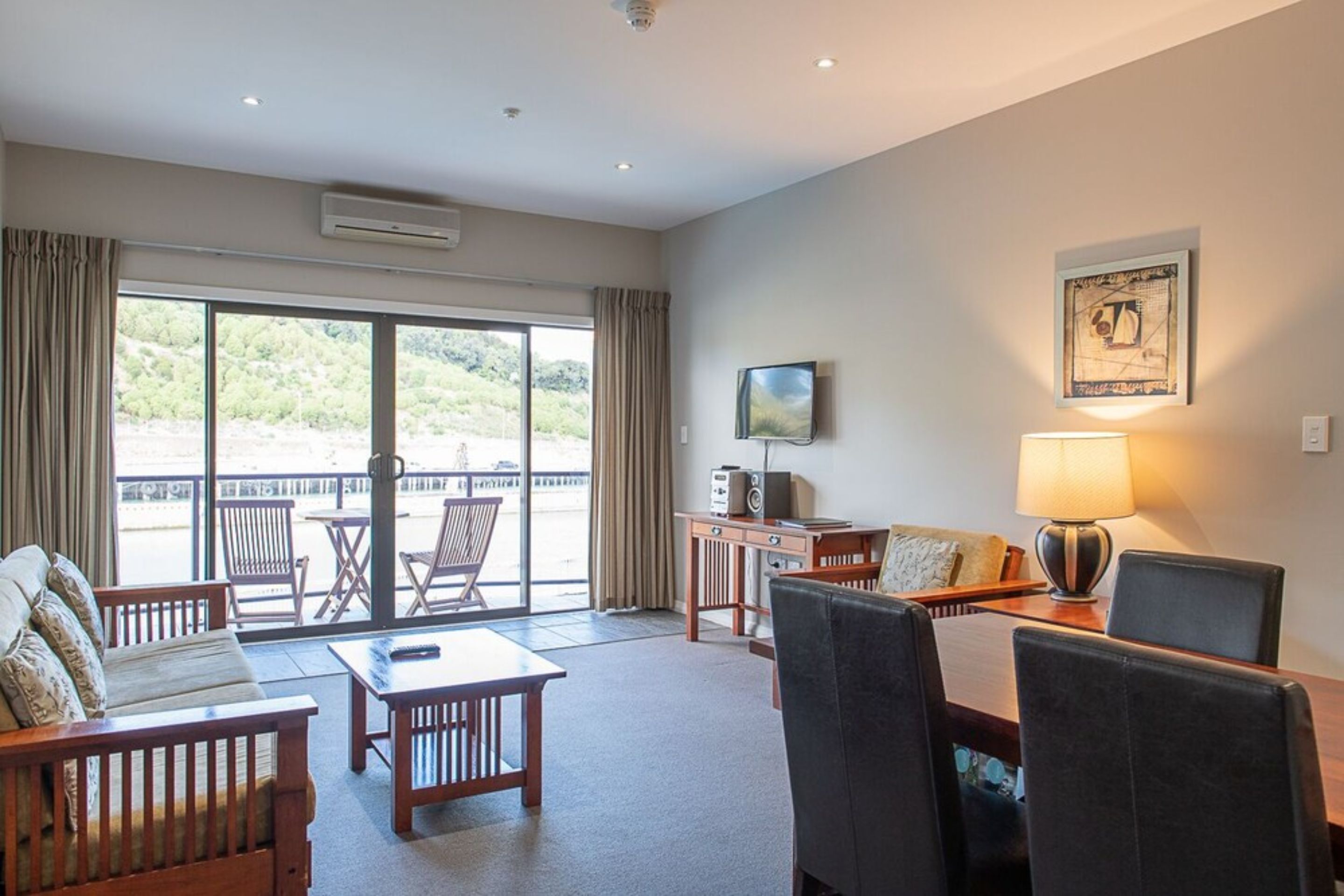 A hotel room with a balcony, a TV, a table, and a sofa.