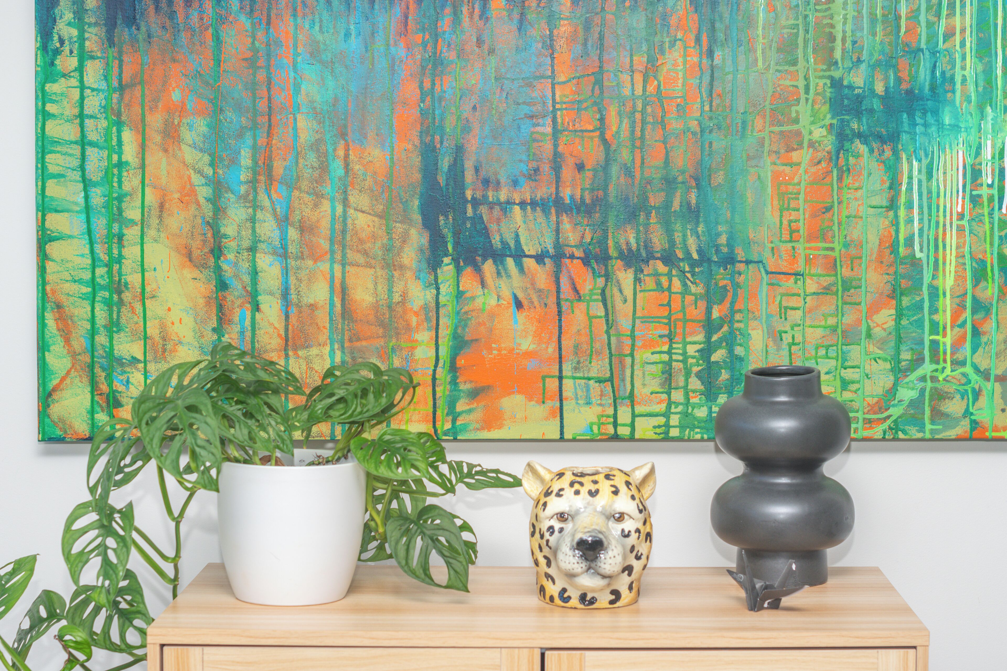 A wooden table with a white pot, a green plant, a ceramic leopard head, and a dark vase.