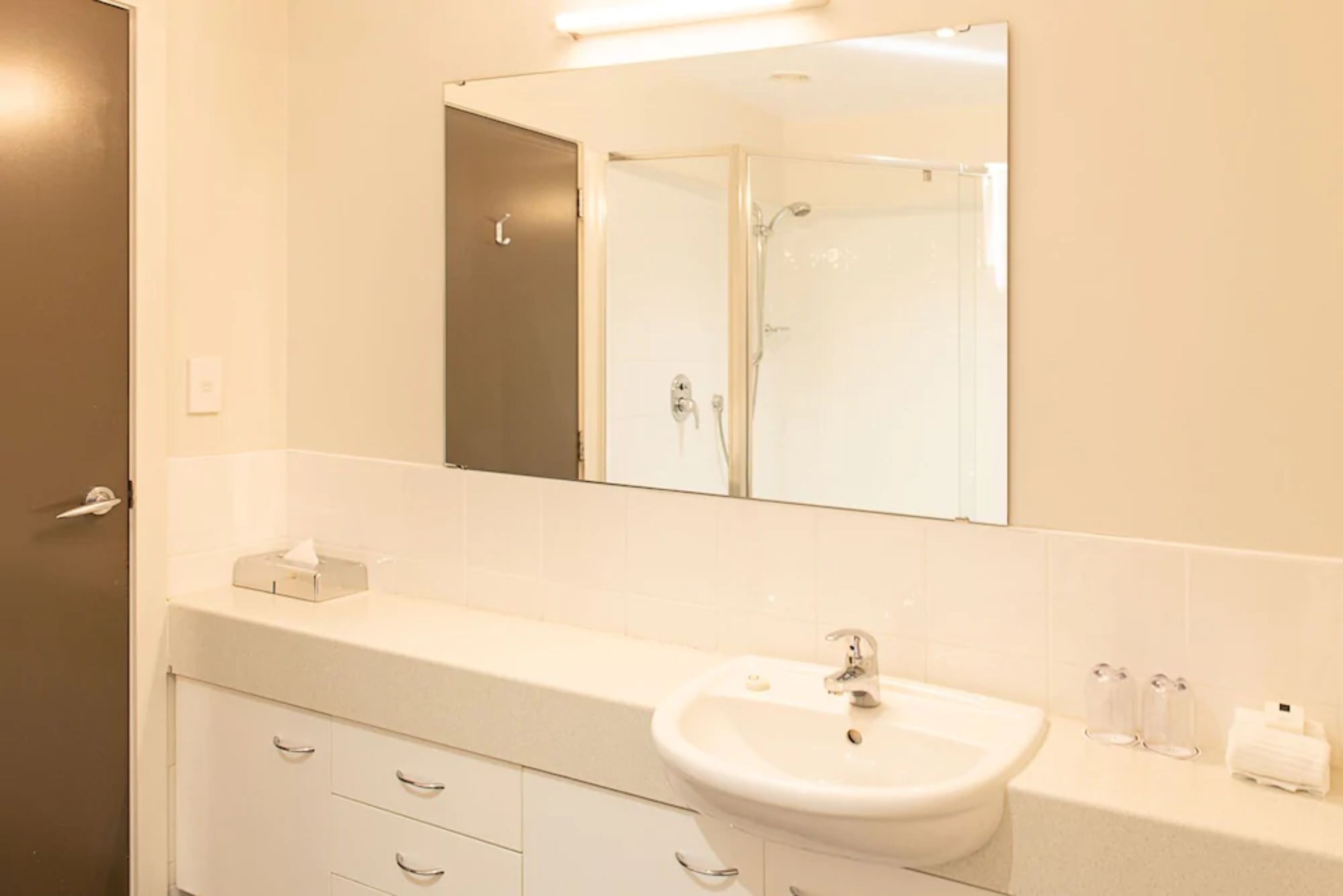 Un baño moderno con un lavamanos blanco, un espejo grande y una ducha.