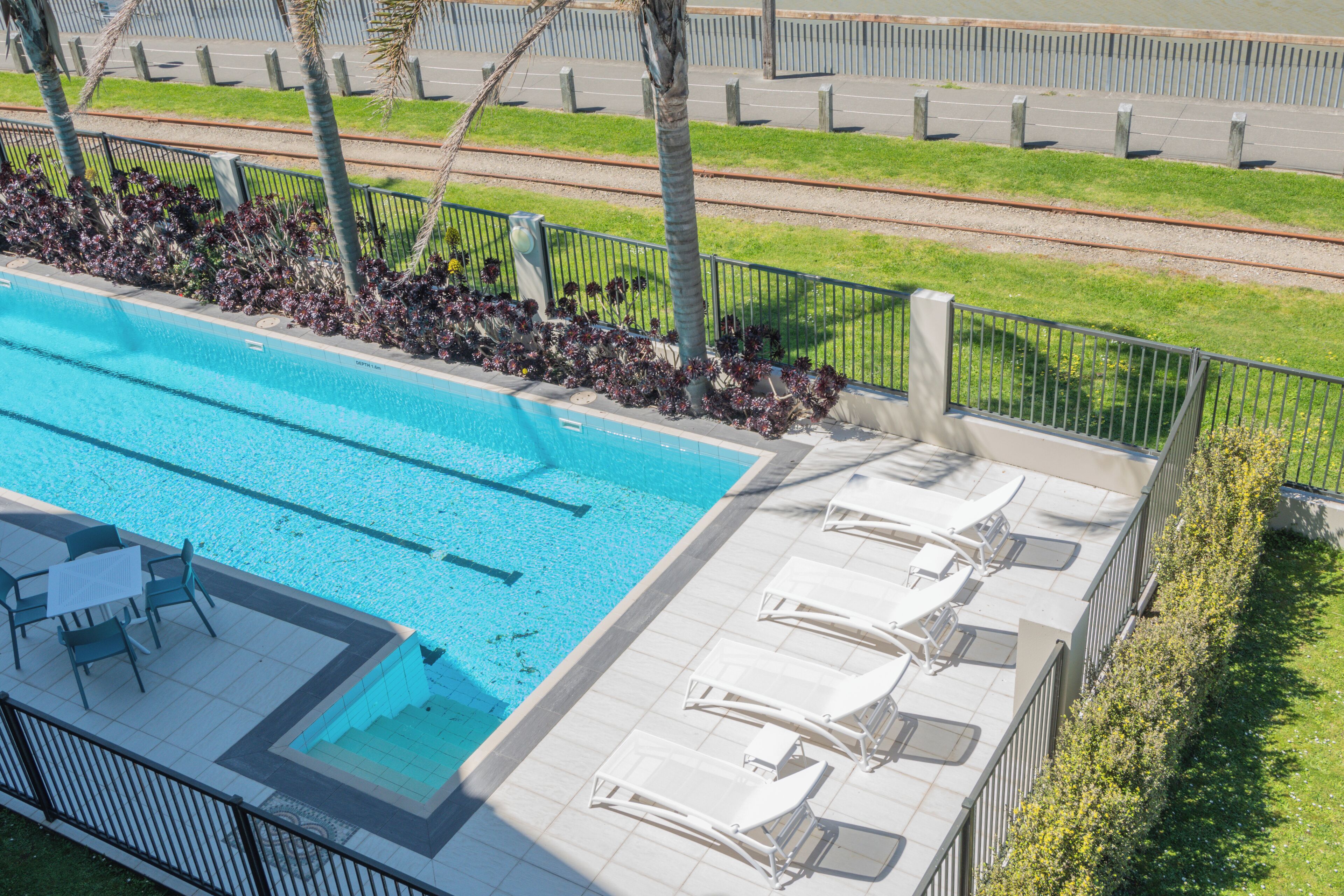 Una piscina con sillas de descanso y un área de terraza con baldosas.