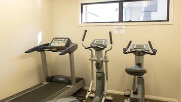A fitness room with a treadmill, elliptical, and stationary bike, a window, and a sign on the wall.