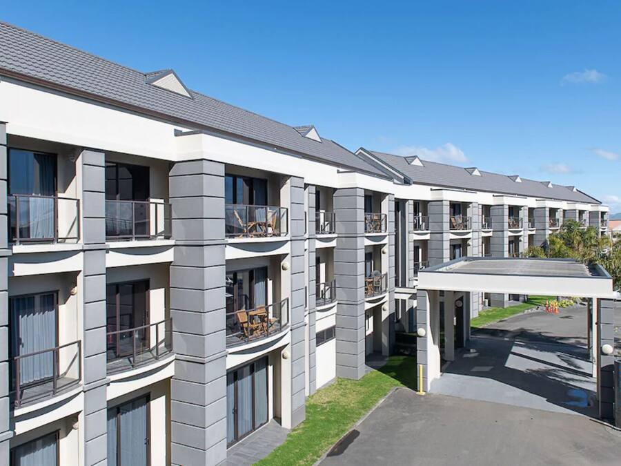 Un hotel de varios pisos con balcones, una entrada cubierta y un área de estacionamiento.