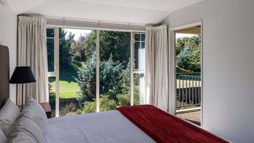 A bedroom with a large bed, a nightstand, a lamp, and a view of a garden through a sliding glass door.
