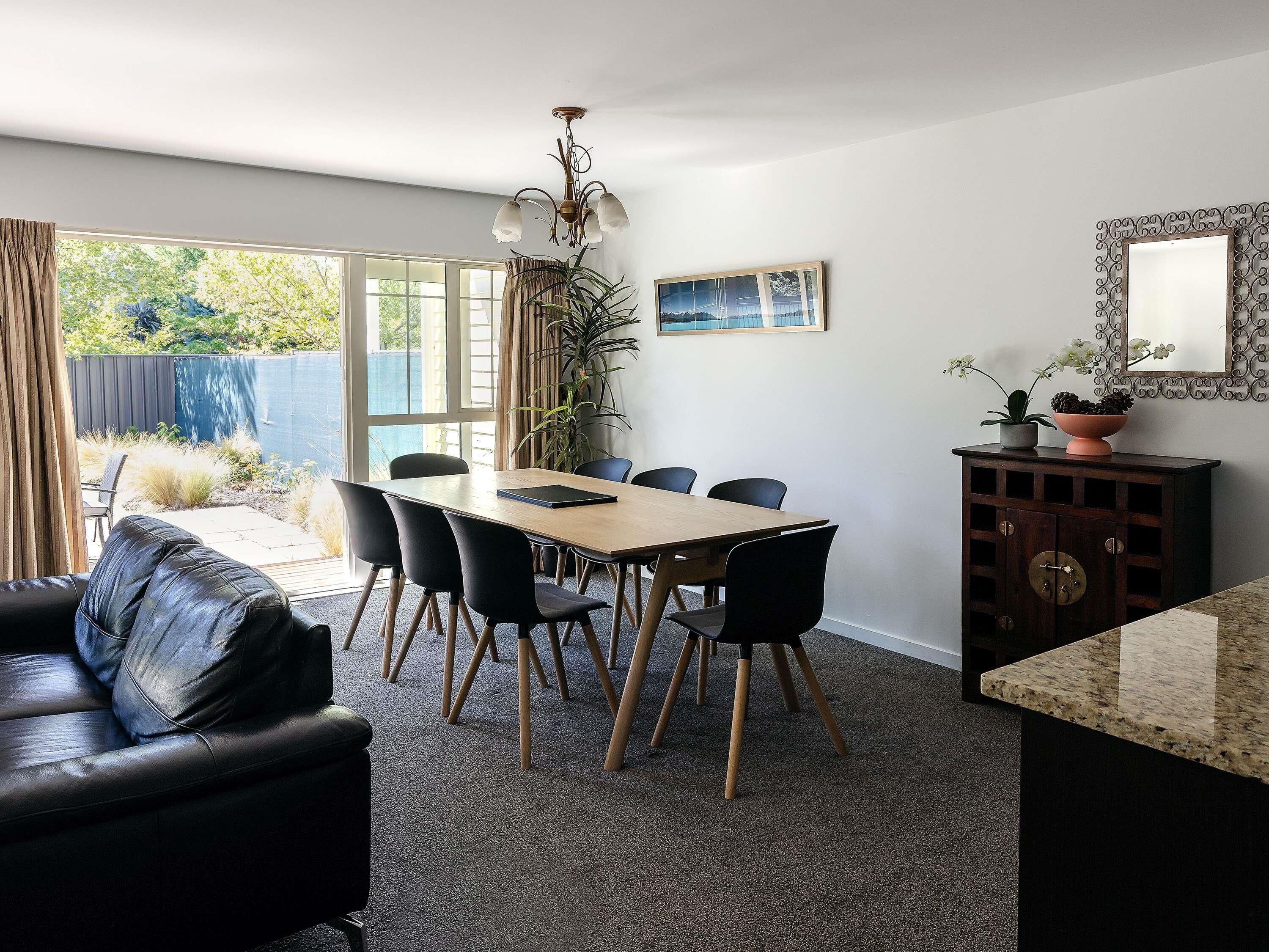 Een eethoek met een tafel, stoelen, een bank, een kast en een groot raam.