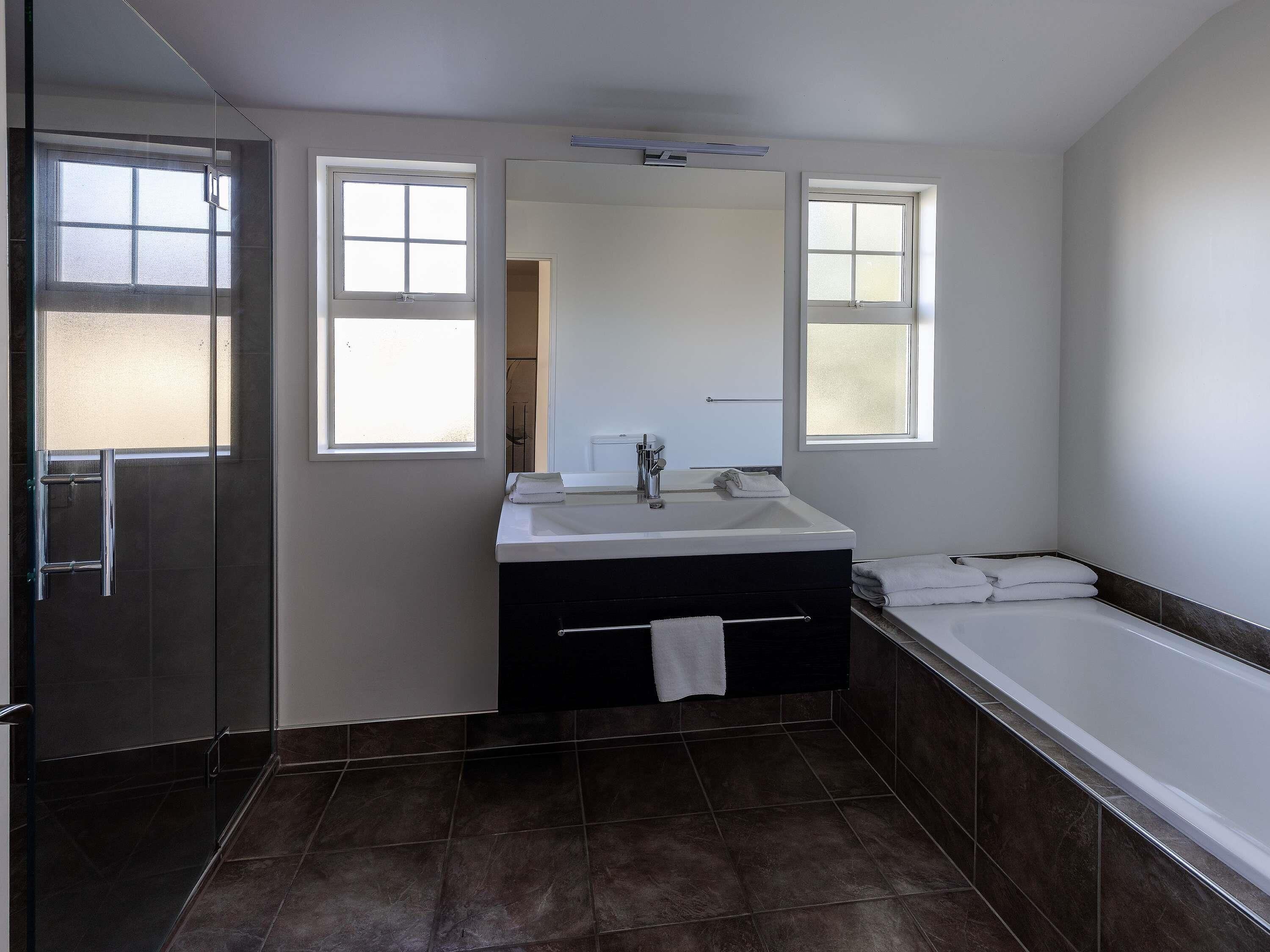 A modern bathroom with a glass shower enclosure, a large mirror, a bathtub, and a vanity with a sink and towel rack.