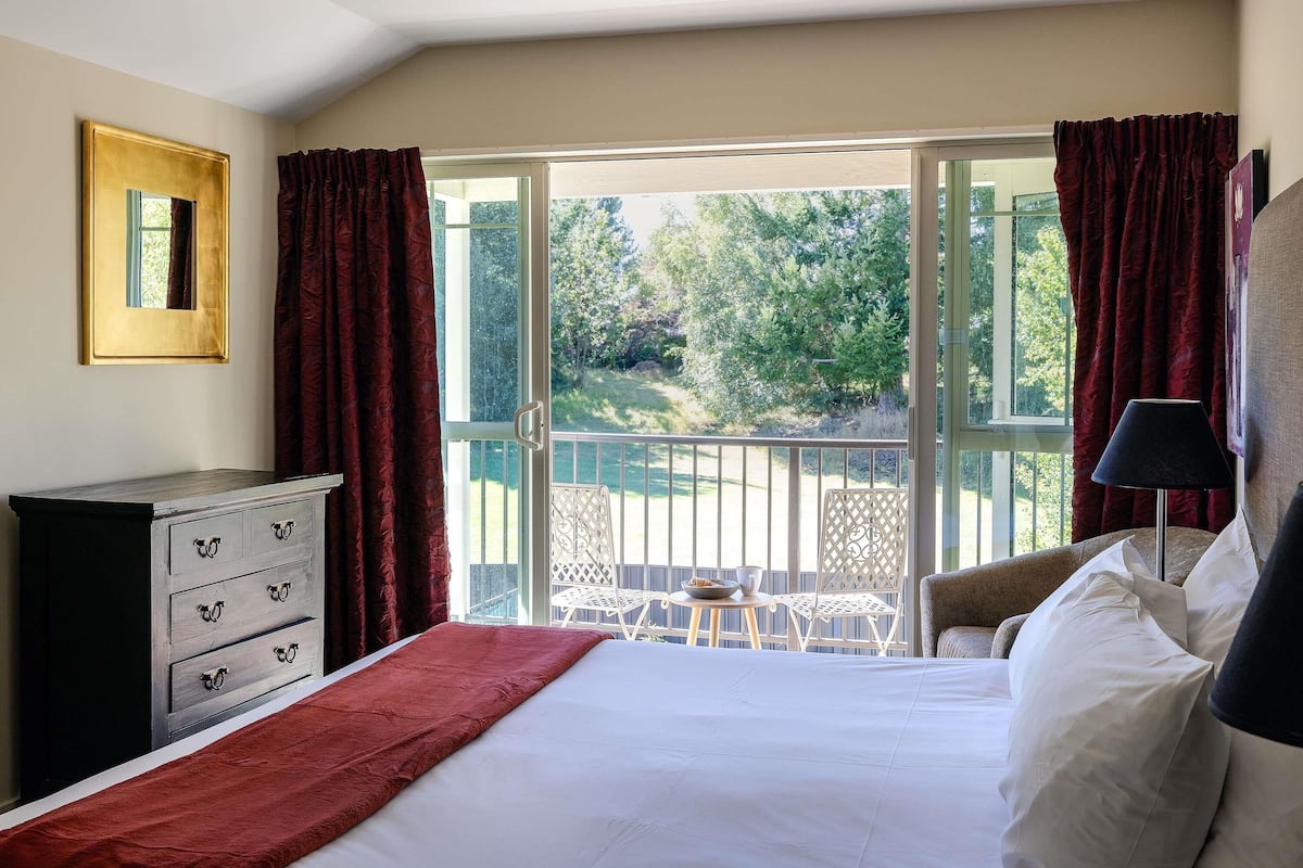 A bedroom with a bed, a dresser, a window with curtains, and a balcony with outdoor furniture.