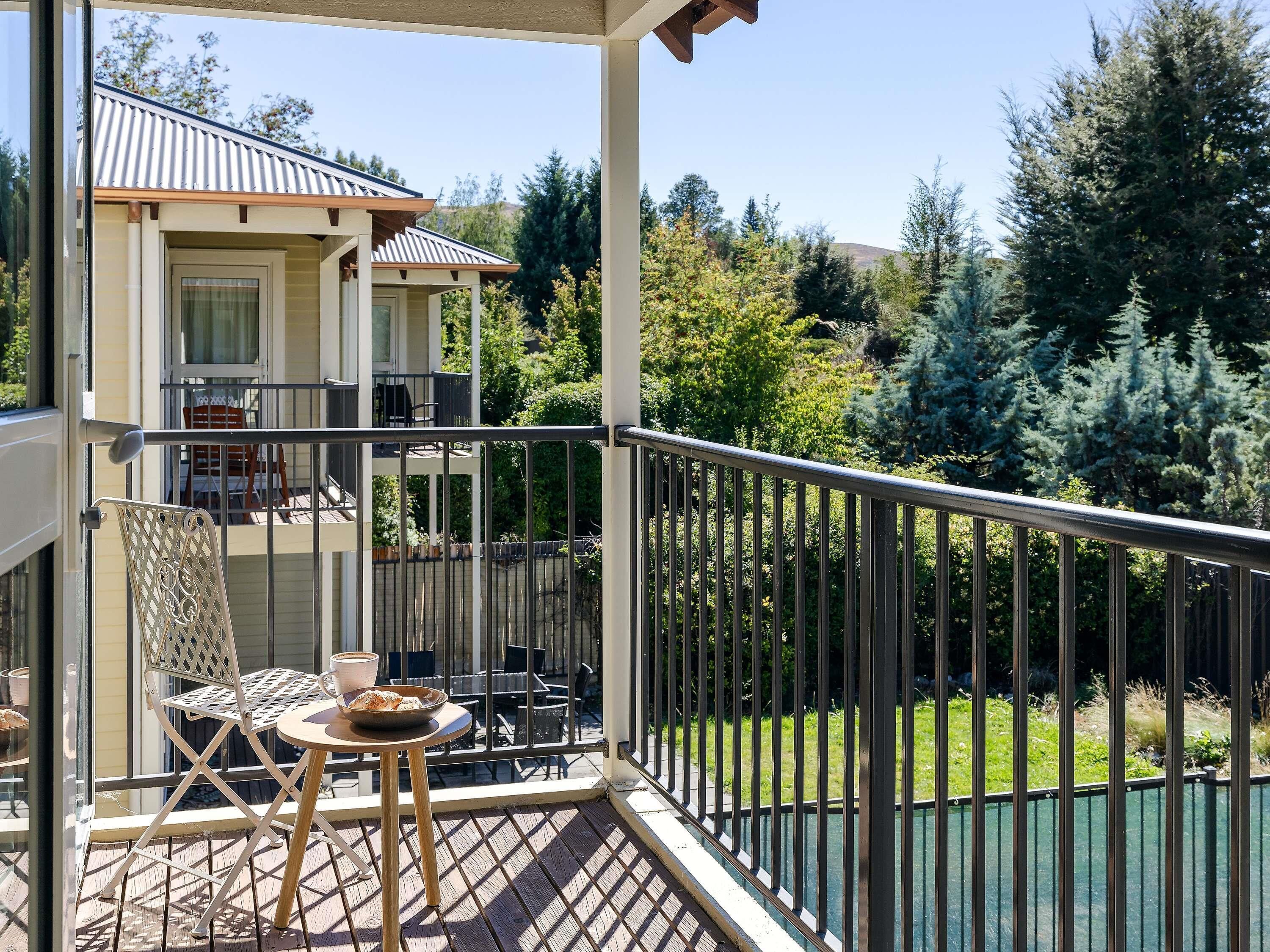 A balcony with a table, chairs, and a railing overlooking a garden and trees.