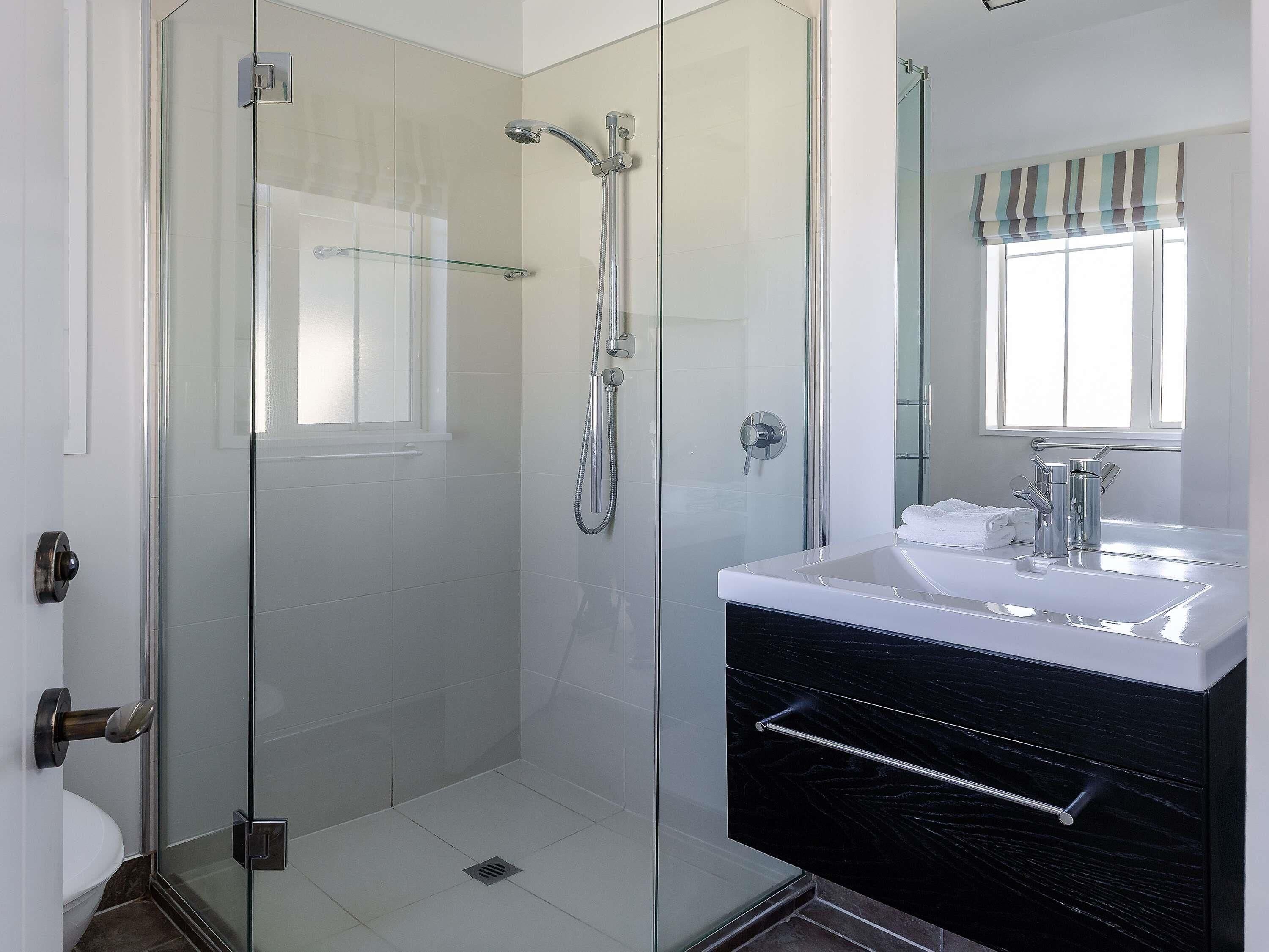 A modern bathroom with a glass-enclosed shower, a white sink with a black cabinet, and a window with a striped valance.
