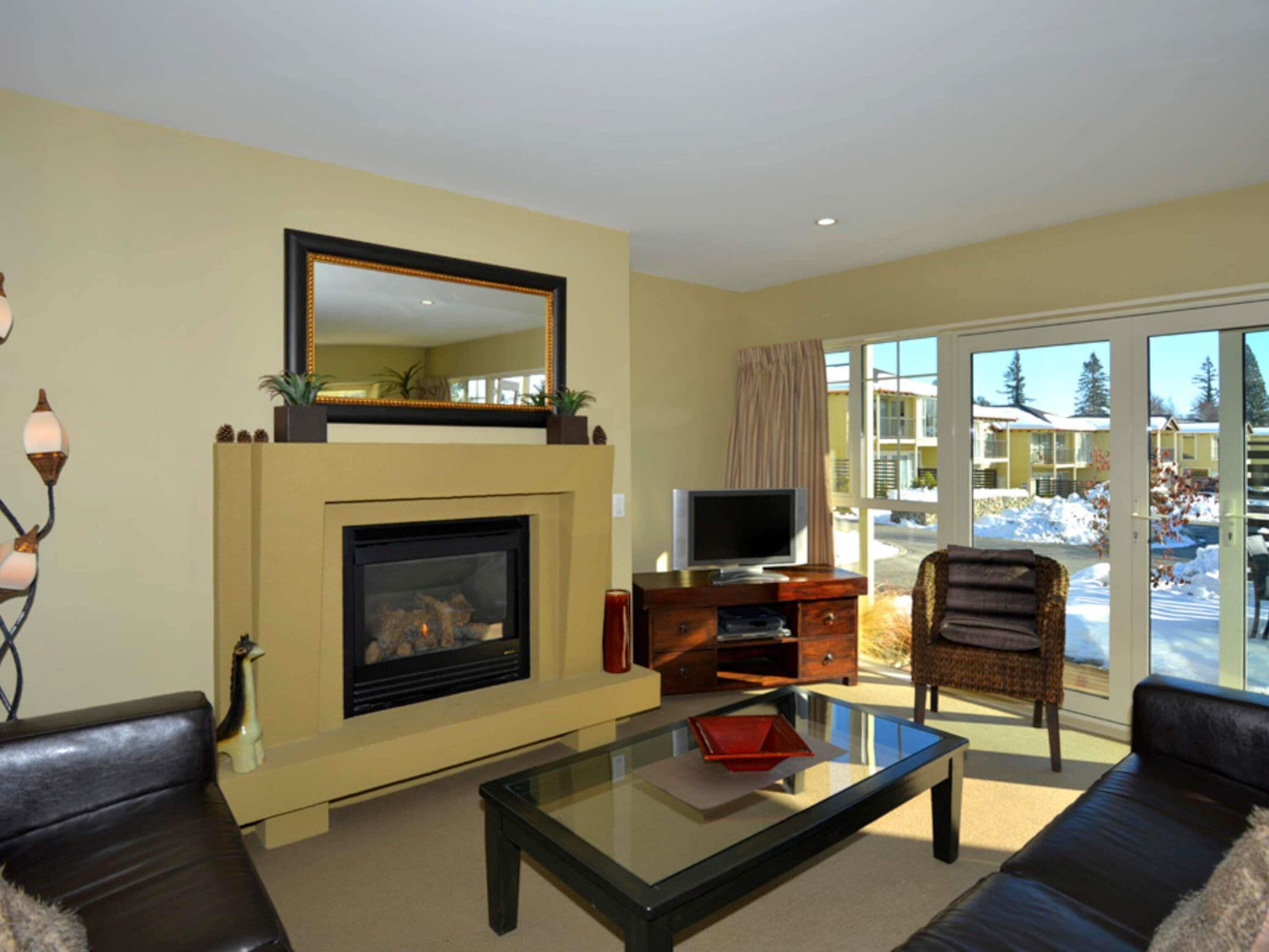 Una sala de estar con chimenea, televisor, una mesa de centro de vidrio y un sofá.