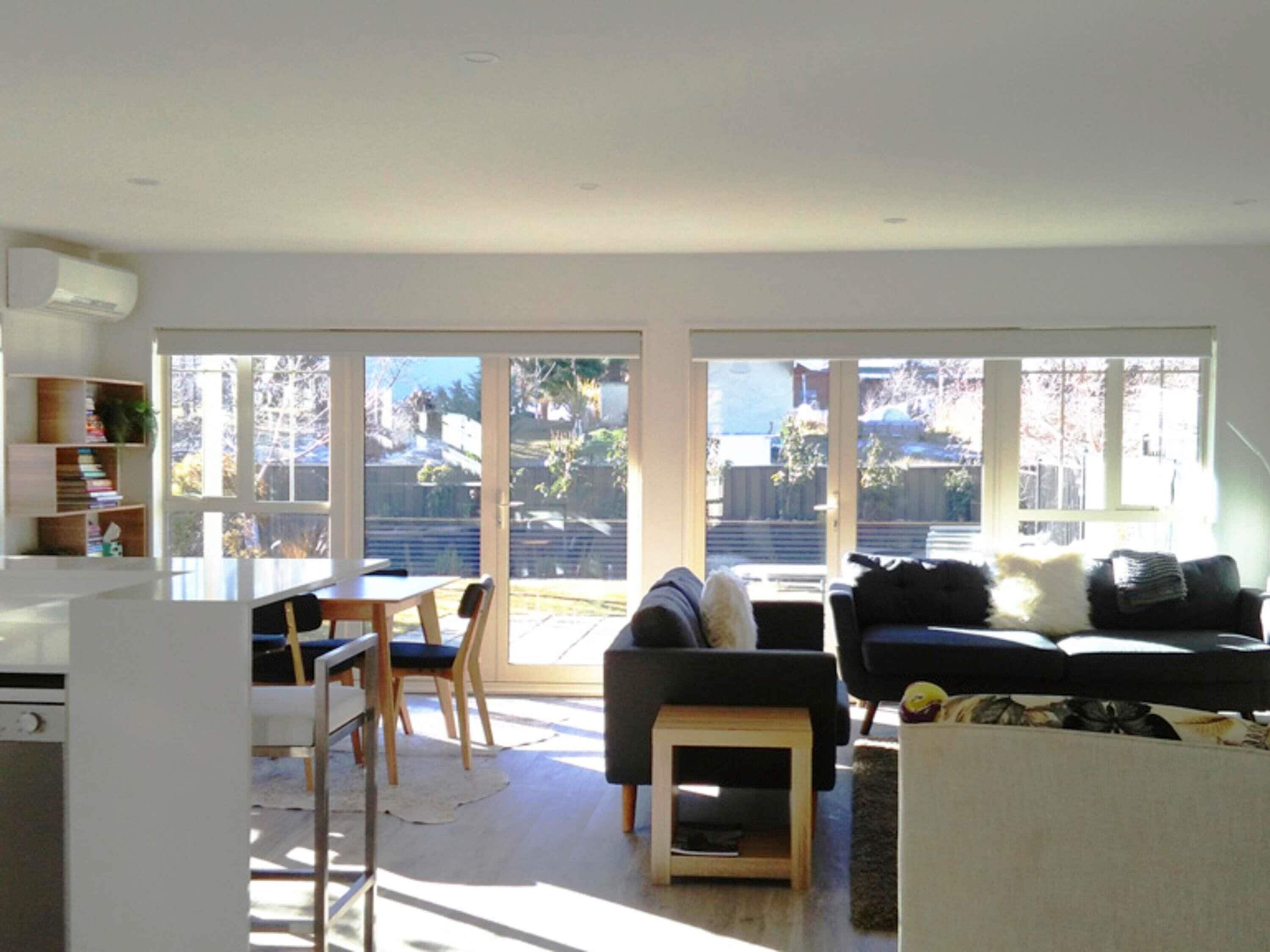 A modern living room with a dining area, large windows, and a view of the backyard.