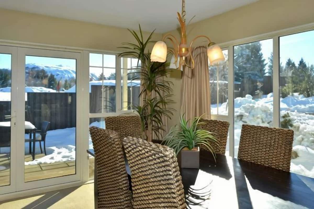 A room with a large sliding glass door, wicker furniture, a potted plant, and a chandelier.