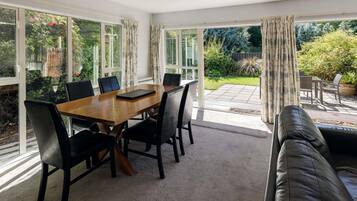 A room with a wooden dining table, black chairs, a leather sofa, and large windows with curtains.