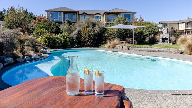 Una piscina con una mesa de madera, una botella y vasos.