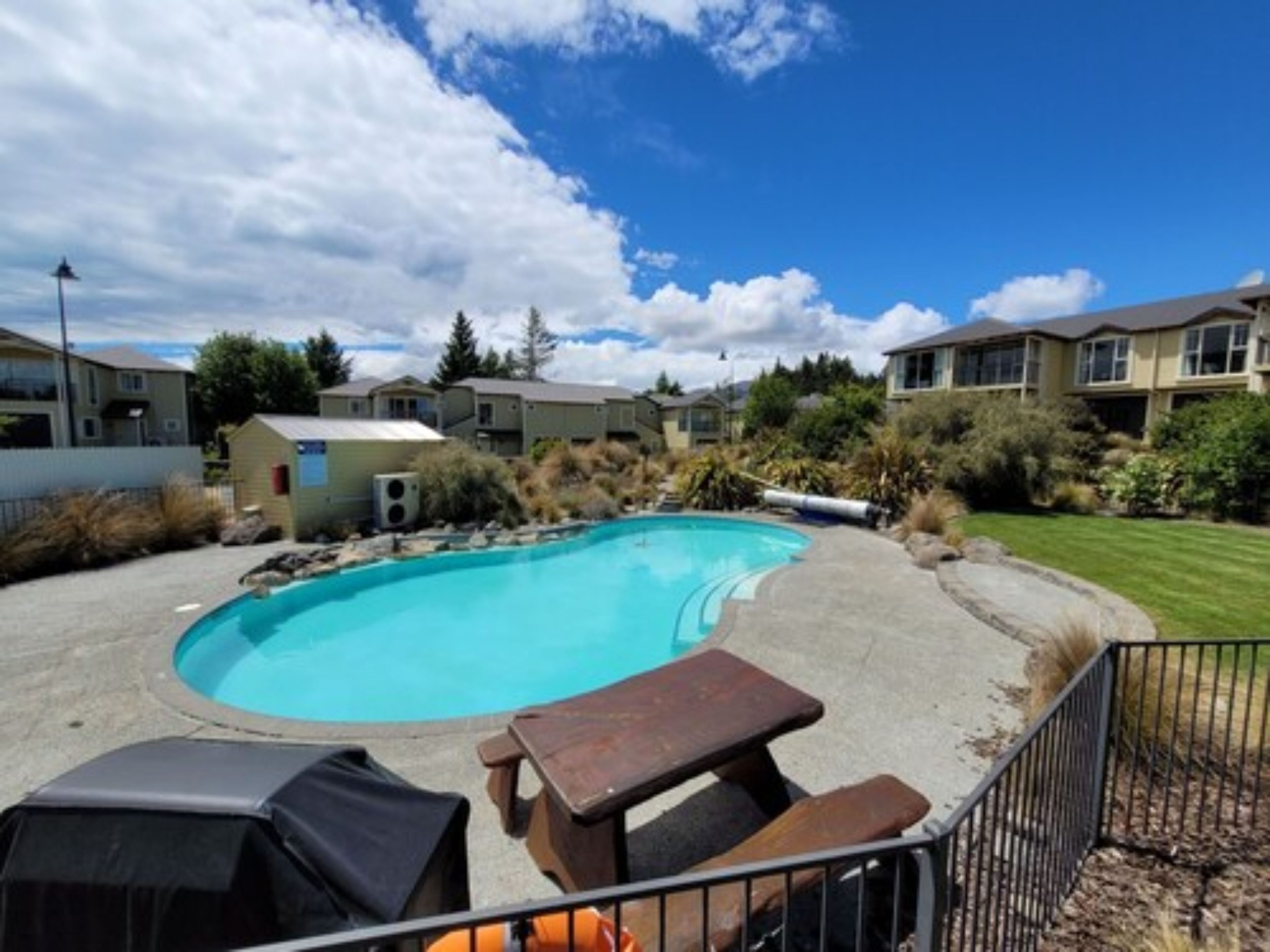 A swimming pool with a patio area, surrounded by residential buildings and greenery.