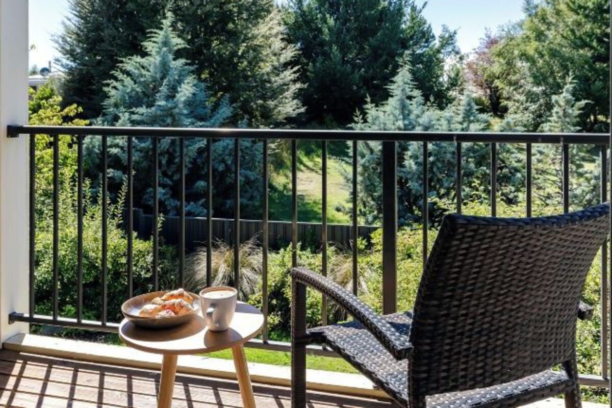 A balcony with a wicker chair and a small table, a bowl of fruit, and a cup of coffee.