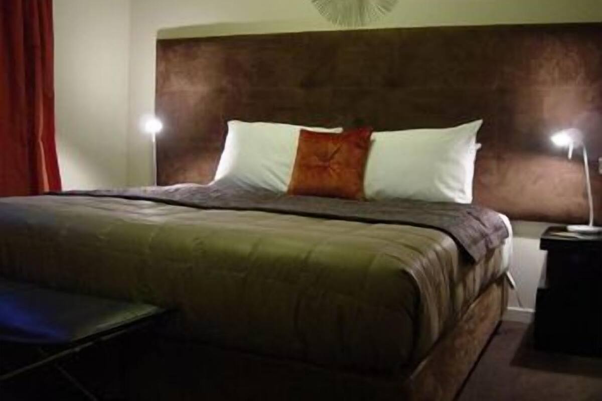 Een hotelkamer met een groot bed, twee bedlampen, een rood gordijn en een ventilator aan de muur.