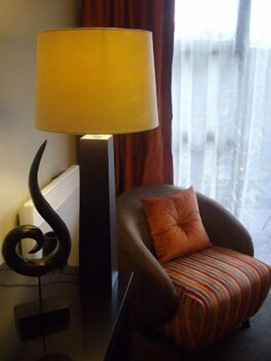 Et moderne værelse med en læderlænestol i mørk farve, en stribet pude, en gul lampe og en dekorativ sort skulptur.