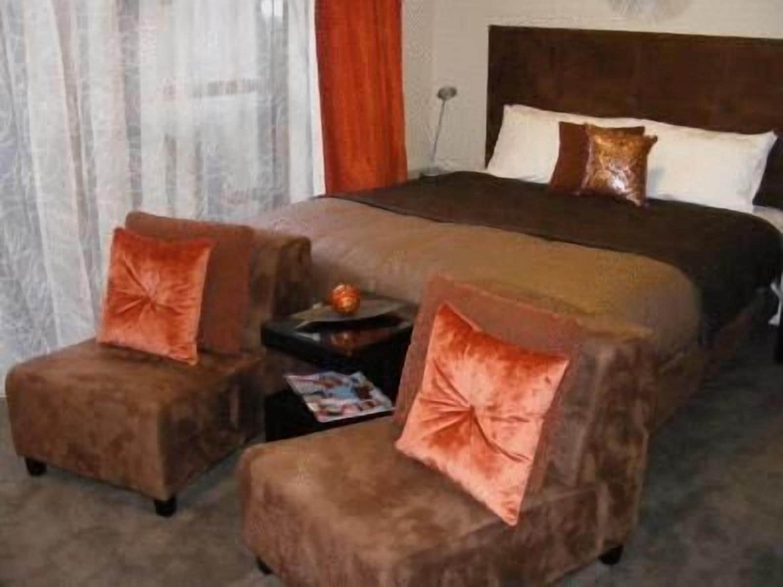 A bedroom with a large bed, two armchairs, a small table, and a nightstand.