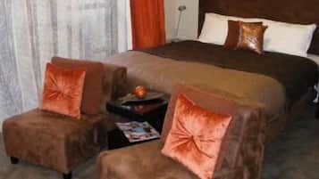 A bedroom with a large bed, two armchairs, a small table, and a nightstand.