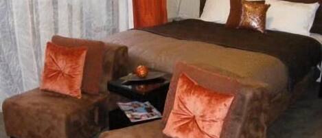 Ein Schlafzimmer mit einem großen Bett, zwei Sesseln, einem kleinen Tisch und einem Nachttisch.