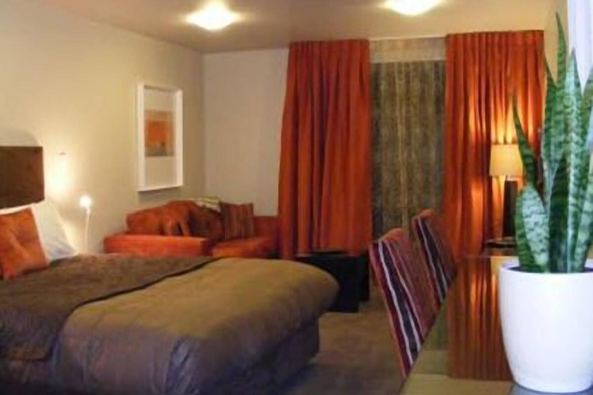 Een hotelkamer met een bed, een tafeltje, een stoel, een kamerplant en gordijnen.