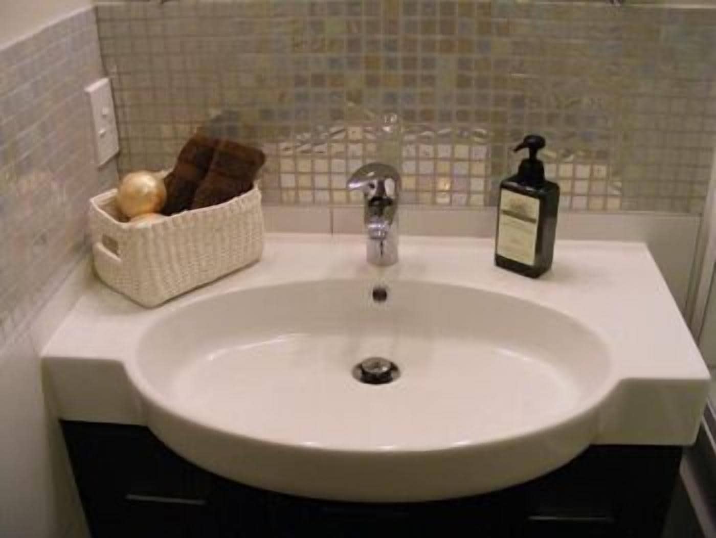 A bathroom sink with a white basin, a silver faucet, a soap dispenser, and a basket with a towel.