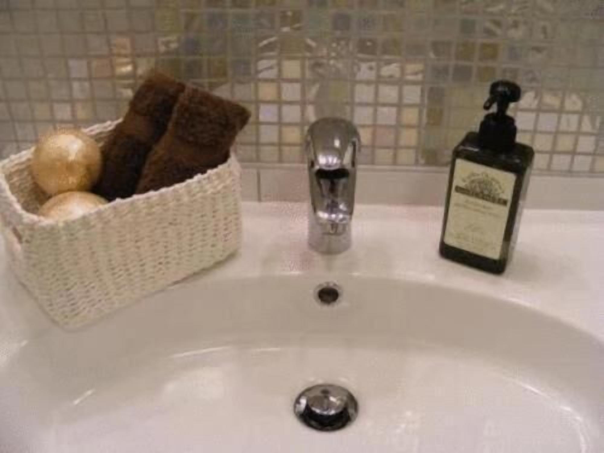 A bathroom sink with a bottle of hand soap, a faucet, and a basket containing a towel and a round object.