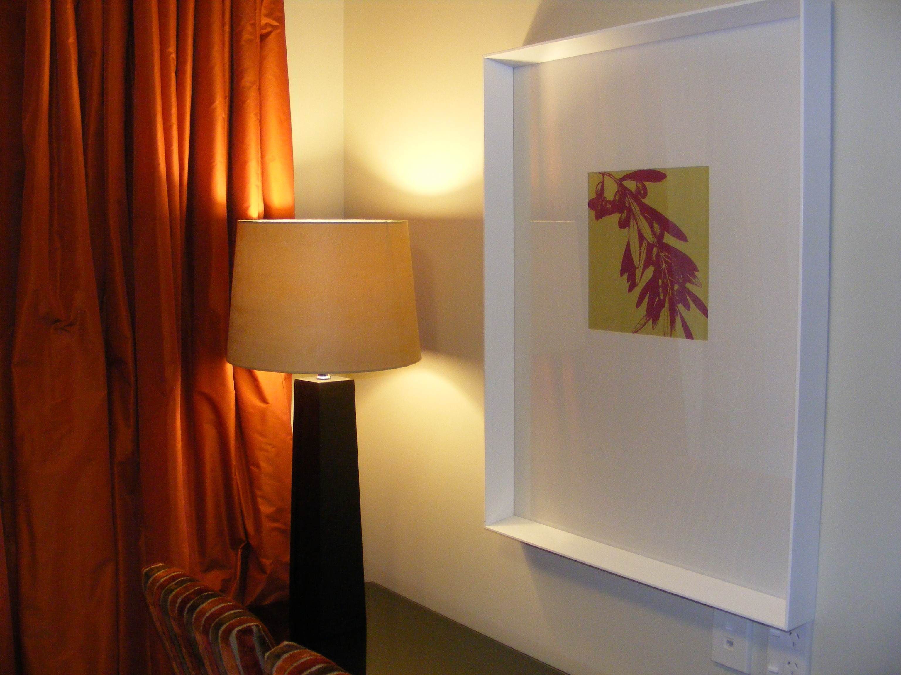 A room with a framed artwork on the wall, a standing lamp, and orange curtains.