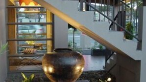 Interior moderno com um vaso grande em pedestal, uma escada e uma janela com vista para o exterior.