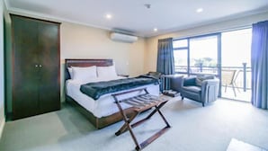 A hotel room with a bed, a seating area with a sofa and armchairs, a balcony with a view, and a wardrobe. - Aotea Motor Lodge (Whanganui)