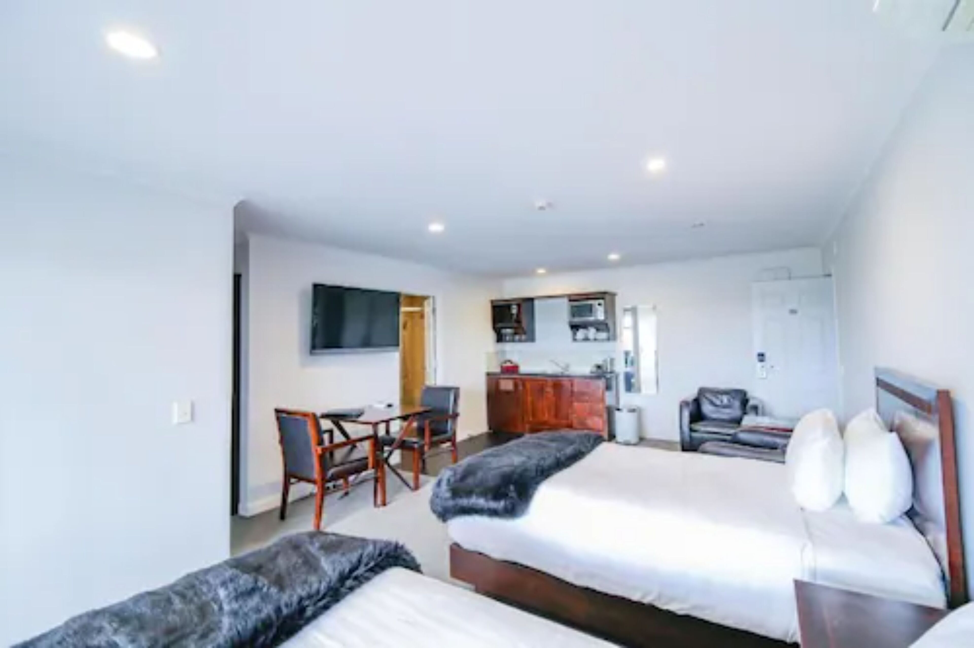 Habitación de hotel con dos camas, un escritorio, una silla, un televisor y una kitchenette.