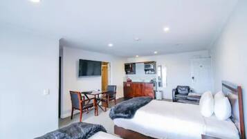 Habitación de hotel con dos camas, un escritorio, una silla, un televisor y una kitchenette.