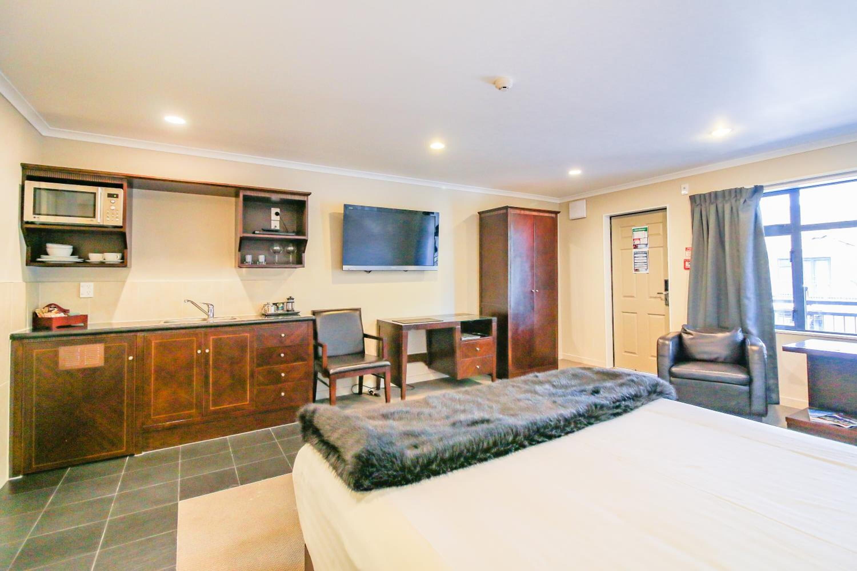 A hotel room with a bed, a desk, a television, a wardrobe, and a window with curtains.