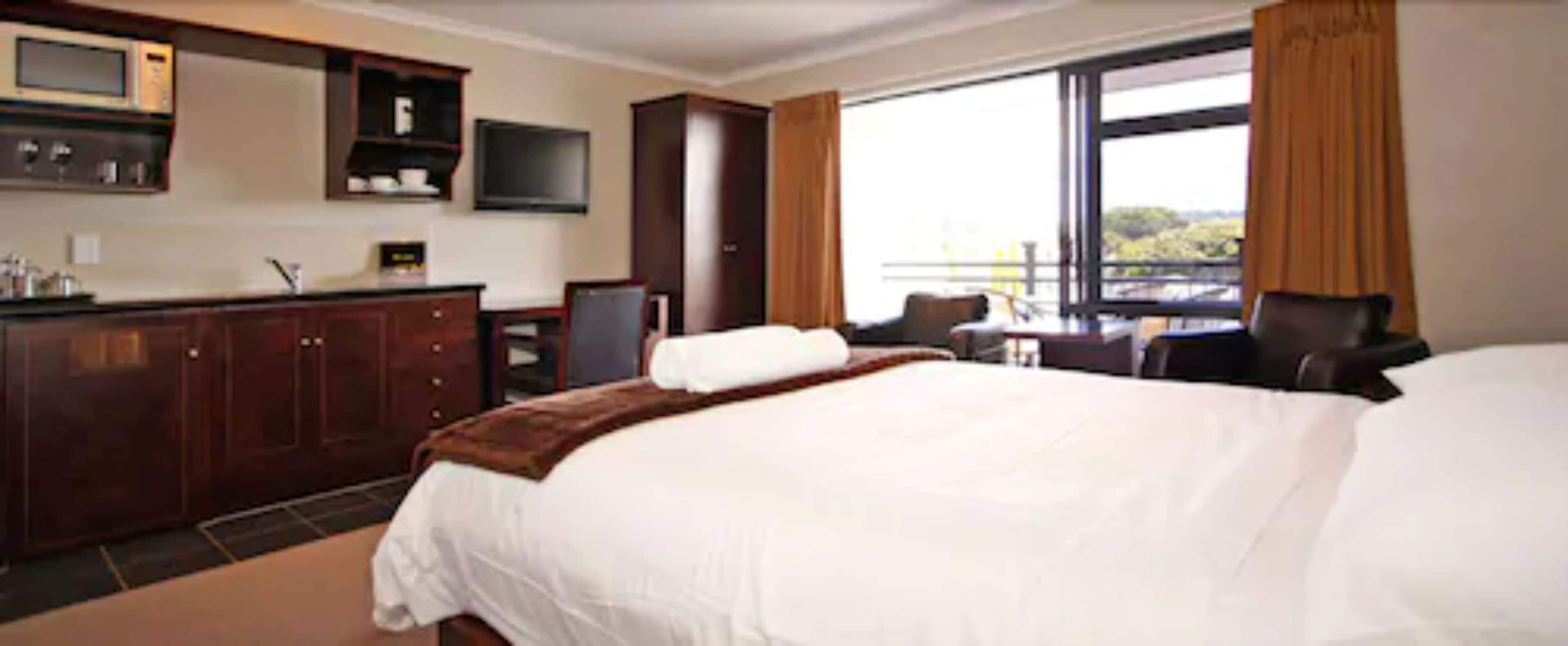 Una habitación de hotel con una cama grande, un escritorio con silla, un televisor sobre el escritorio y una ventana con cortinas.